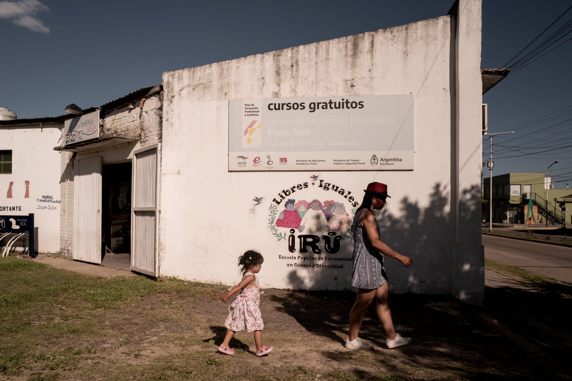 A woman and child walk past a building with weathered signage.
